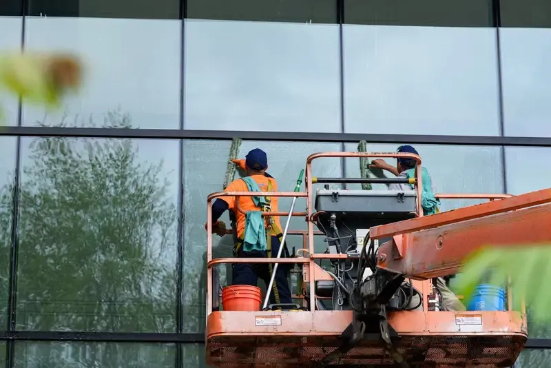 Workers cleaning large windows on a building using a cherry picker.