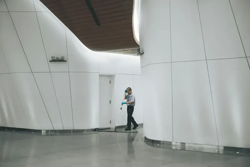 Janitor cleaning a modern, minimalist hallway with white walls.